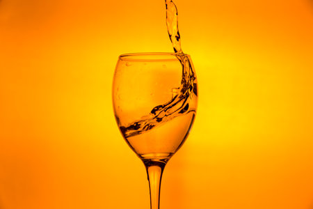 Wineglass with splashing drops of fresh water - motion freeze close-up picture isolated on the orange background.の写真素材