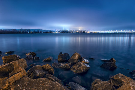 Night in Kiev over the Dnipro river - city lights and dark river. Long exposure photo.
