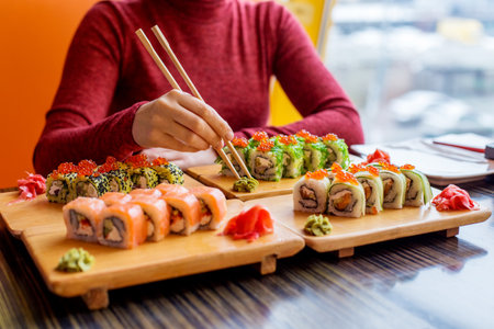 Woman eating sushi rolls at the table - close up photo. Traditional Japanese oriental kitchen with raw fish.の写真素材