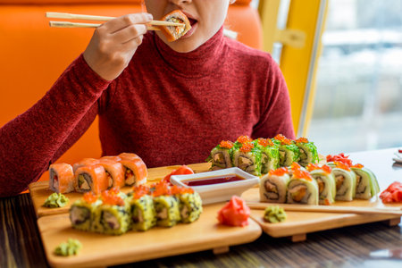 Woman eating sushi rolls at the table - close up photo. Traditional Japanese oriental kitchen with raw fish.の写真素材