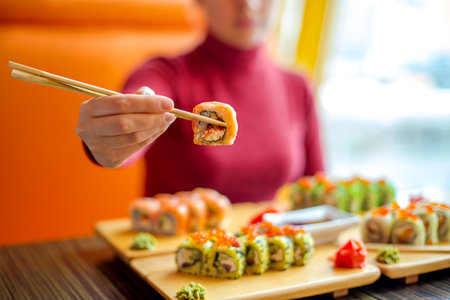 Woman eating sushi rolls at the table - close up photo. Traditional Japanese oriental kitchen with raw fish.の写真素材