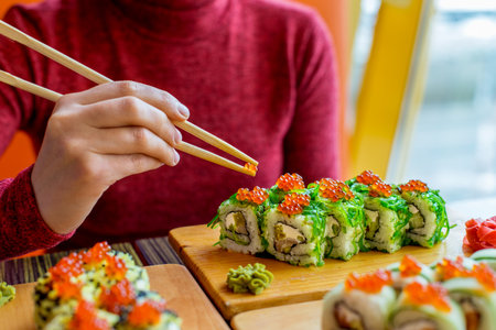 Woman eating sushi rolls at the table - close up photo. Traditional Japanese oriental kitchen with raw fish.の写真素材