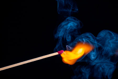 Burning match isolated on black background with smoke clouds. Macro photo.