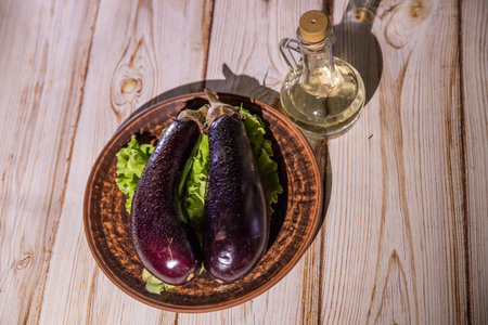 Two big eggplants on the green salad leaves in the plate on the wooden tableの写真素材