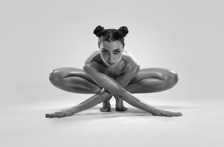 Beautiful nude sexy fitness girl with great figure flexing her perfect body in a yoga pose at the studio. Spider pose. Black and whiteの写真素材