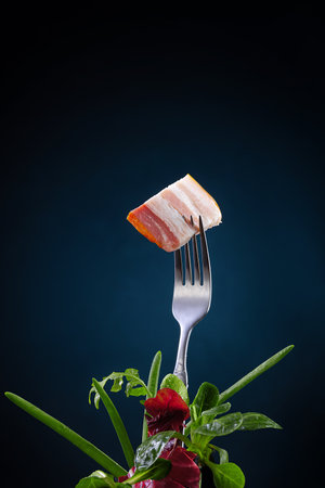 Fork with pork bacon - Ukrainian traditional dinner snack with onion and herbs on the dark blue background. Close-up food product photo.の写真素材
