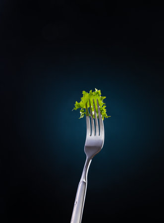 Fork with fresh green salad leaves pinned on the black background. Close-up food product photo.の写真素材