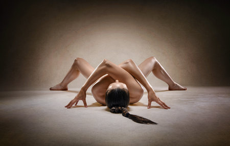 Beautiful nude sexy fitness girl with great figure flexing her perfect body in a yoga pose at the studio. Spider pose.の写真素材