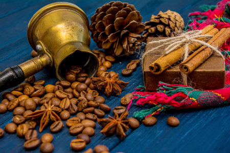 Coffee beans, anise, cinnamon, turk, present box and cones on dark blue wooden background. Christmas evening backgroundの写真素材