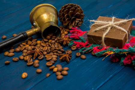 Coffee beans, anise, cinnamon, turk, present box and cones on dark blue wooden background. Christmas evening backgroundの写真素材