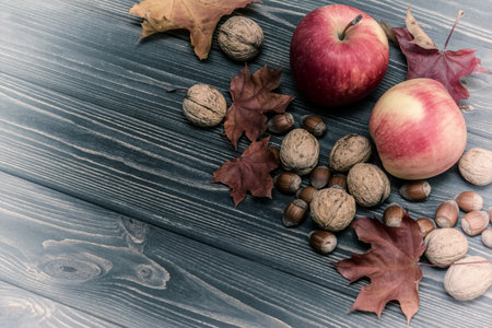 Apples, nuts, berries with maple leaves on wooden background. Autumn card. Vintage effectの写真素材