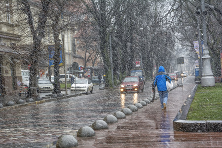 Lviv, Ukraine - December 12, 2016: Snowstorm with wet heavy snow and wind. Street view with cars and a lonely pedestrianのeditorial素材