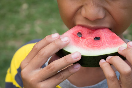 Close up of the boy is eating watermelon on green nature background.の写真素材