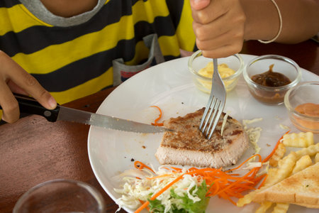 A boy is Eating steak in a restaurant.の写真素材