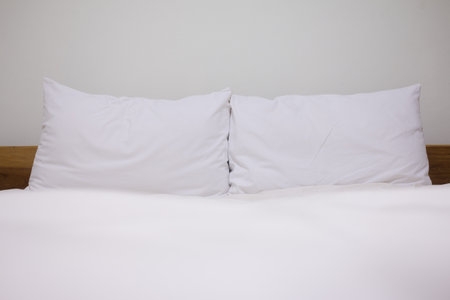Close up white pillow and bedding sheets on natural white wall bedroom background, Messy bed concept.の写真素材