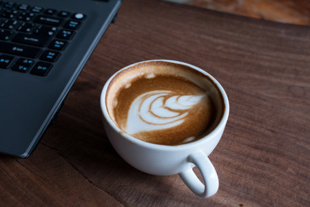 Close up of Cup of hot latte art coffee with laptop computer on wooden table, work with coffee...