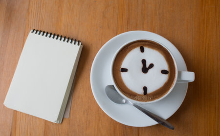 Close up of A Cup hot latte art coffee drawn an oclock business concept on wooden table with note book.の写真素材