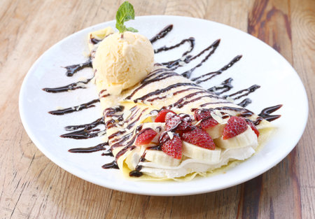 Closeup of vanilla ice cream with crepes and strawberry on wooden desk.の写真素材