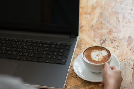 A Business woman is holding a white coffee cup during work with laptop-PC on office table.の写真素材