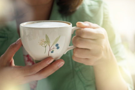 A woman holding a cup of hot latte coffee in warm morning day.の写真素材