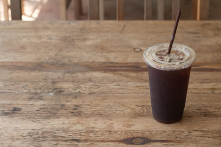 Americano iced coffee in takeaway plastic cup on wooden desk in coffee's shop.