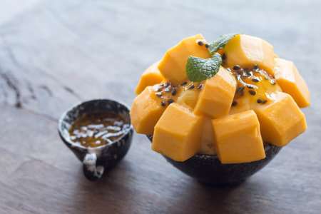Refreshing mango ice cream and passion fruit in ceramic bowl on wooden desk for favorite summer dessert.の写真素材