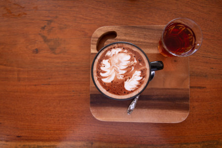 Piccolo Latte art in small glass with hot tea on wooden desk.