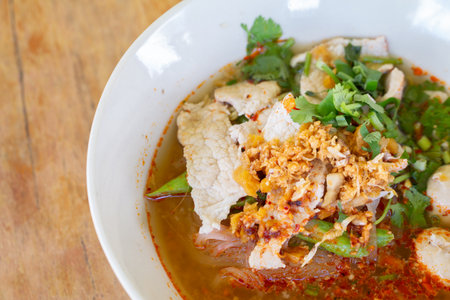 Rice noodle in spicy soup with pork ball, vegetable and pork serving on wooden desk in canteen.