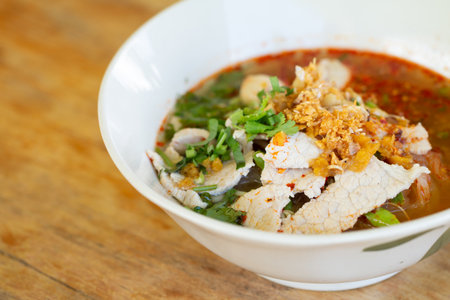 Rice noodle in spicy soup with pork ball, vegetable and pork serving on wooden desk in canteen.の写真素材