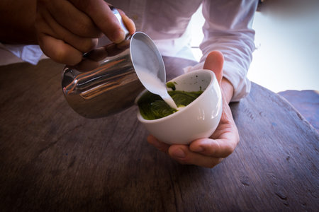 Barista pouring milk in coffee cup make green tea late art.の写真素材