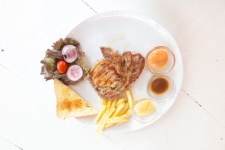 Flat lay views of Pork chop steak with white plate on vintage wooden desk.の写真素材