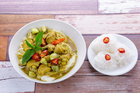 Green curry chicken with rice noodles on wooden table