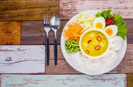 Thai rice noodle with curry sauce on white plate wooden background
