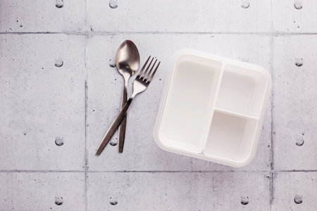 Empty white plastic food container with spoon and fork on wooden tableの写真素材