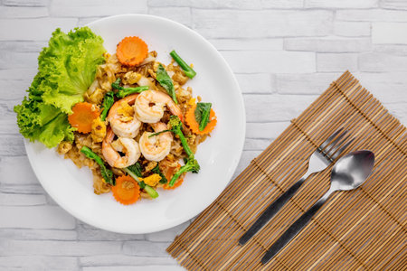 Stir-fried rice noodles with soy sauce and shrimp on wooden background