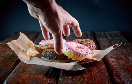 the human hand takes a sweet fried donut from the wood tableの写真素材