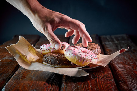 the human hand takes a sweet fried donut with sweet sugar coating from the wood tableの写真素材