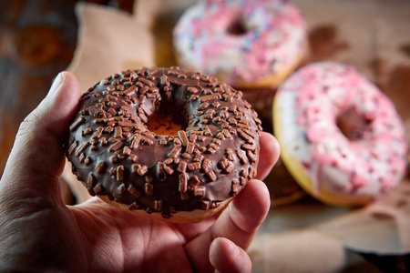 the close-up of a chocolate donut in a human hand, blurred backgroundの写真素材