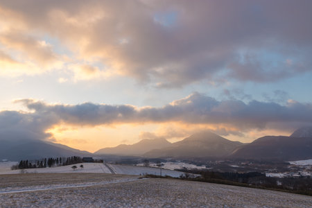 Winter landscape with snow covered fields and mountains in the background at sunsetの写真素材