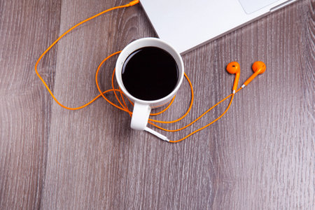 Wood table with laptop, earphone and a cup of coffee. Warm tone. Focused on the coffee cup.の写真素材