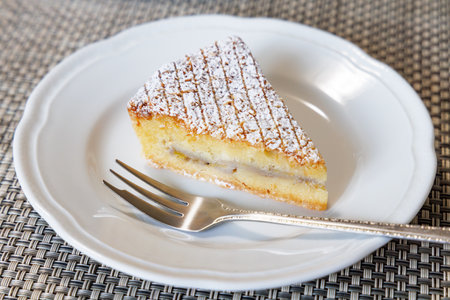 A piece of almond cake on a white plate with a fork.の写真素材