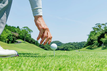 Hands placing a golf ball on a tee on a teeing ground with fresh greeneryの写真素材