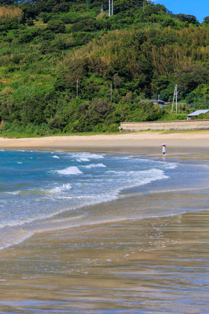A young woman walks along the beach on a sunny summer day.の写真素材