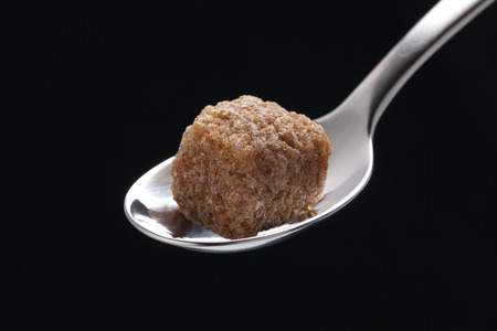the cubes of brown sugar in a silver spoon, isolated on blackの写真素材