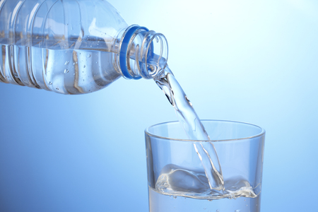 Pouring glass of water from plastic bottle on blue backgroundの写真素材