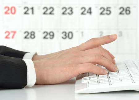 A businessman working on a computer in front of a calendarの写真素材