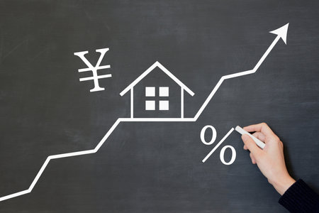 A person's hand draws an image of rising housing prices and interest rates on a blackboardの写真素材