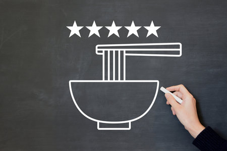 A man's hand drawing a five-star rating and a picture of ramen on a blackboardの写真素材