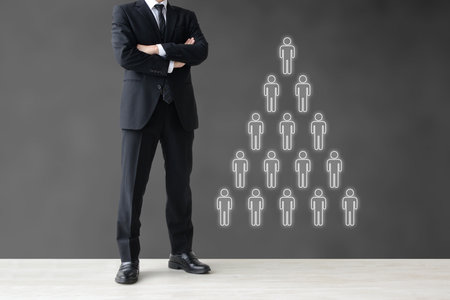 A businessman with his arms folded and a pyramid-shaped organizational chart - an image to think about in relation to human resourcesの写真素材
