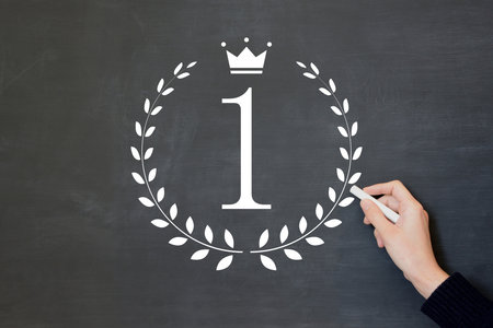 A man's hand drawing the number 1 surrounded by a laurel wreath on a blackboardの写真素材